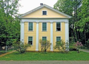 A yellow Greek Revival home with white trim that accentuates the period pilasters.